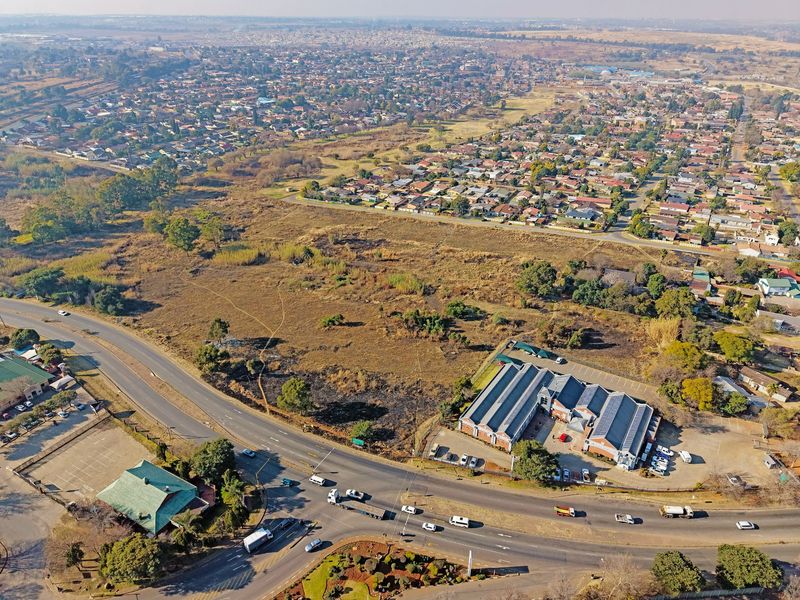Aerial view of a large vacant residential land parcel situated near a main road and existing commercial infrastructure.