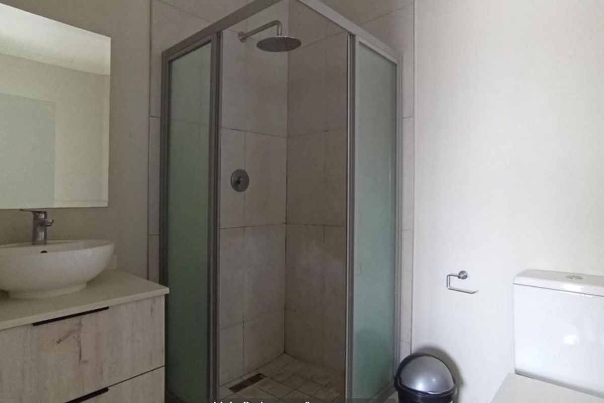 A modern bathroom featuring a corner shower enclosure with a rain shower head, a vessel sink on a vanity cabinet, and a standard toilet.