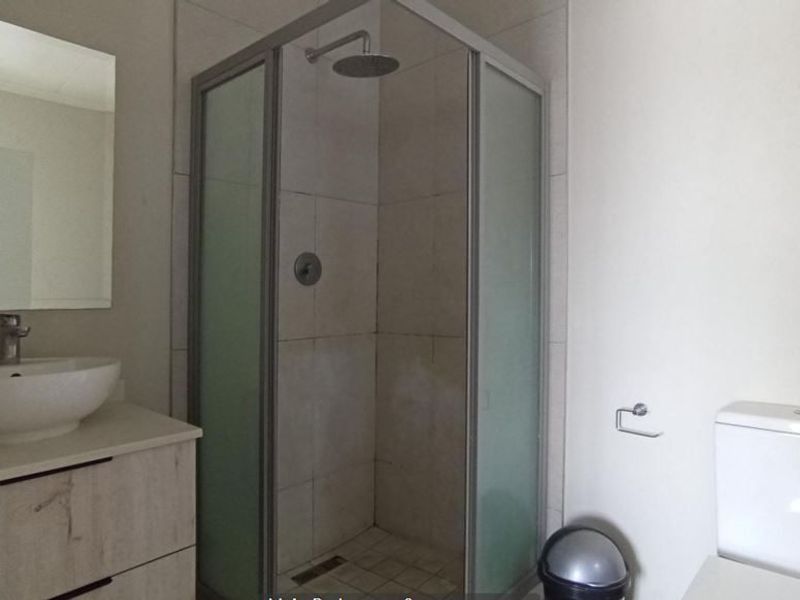 A modern bathroom featuring a corner shower enclosure with a rain shower head, a vessel sink on a vanity cabinet, and a standard toilet.