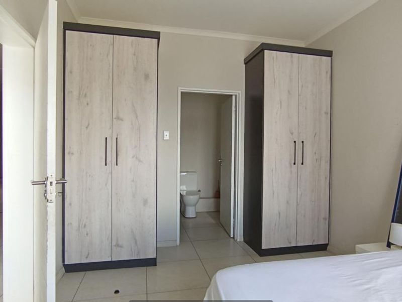 A well-maintained bedroom featuring modern built-in cupboards, neutral tiled flooring, and direct access to an en-suite bathroom.