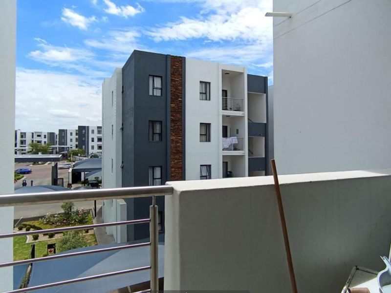 A balcony featuring a stainless steel balustrade and concrete parapet wall, offering views of the surrounding apartment complex and grounds.