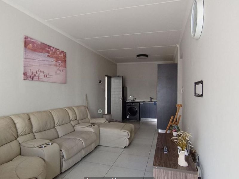 Open-plan living area featuring tiled flooring and a compact kitchen corner with built-in cabinetry and sink.