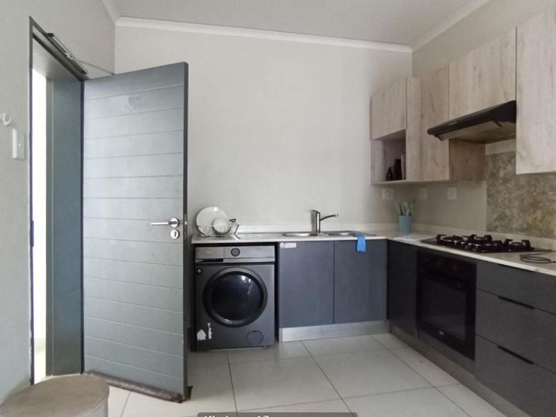 Modern kitchen featuring two-tone cabinetry, integrated oven, gas hob, extractor fan, and tiled flooring with a dedicated space for a washing machine.