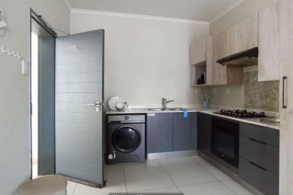 Modern kitchen featuring two-tone cabinetry, integrated oven, gas hob, extractor fan, and tiled flooring with a dedicated space for a washing machine.