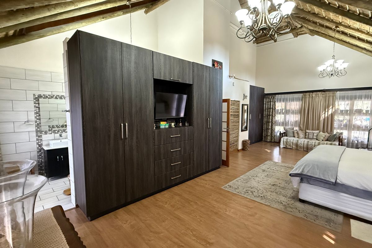 Spacious bedroom featuring high vaulted timber ceilings, exposed beams, built-in dark wood cabinetry, and an integrated en-suite bathroom area with modern tiling.