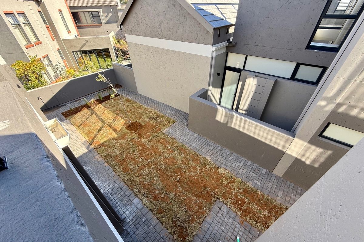 A rear courtyard area featuring paved flooring and a small garden section, enclosed by boundary walls within a townhouse complex.