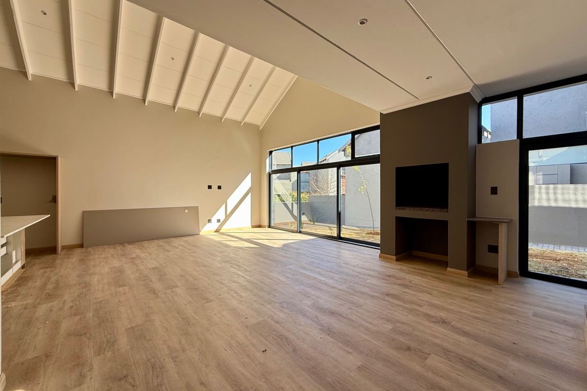 Spacious, light-filled living area featuring a high vaulted ceiling, modern laminate flooring, a built-in fireplace, and large sliding doors opening to the exterior.