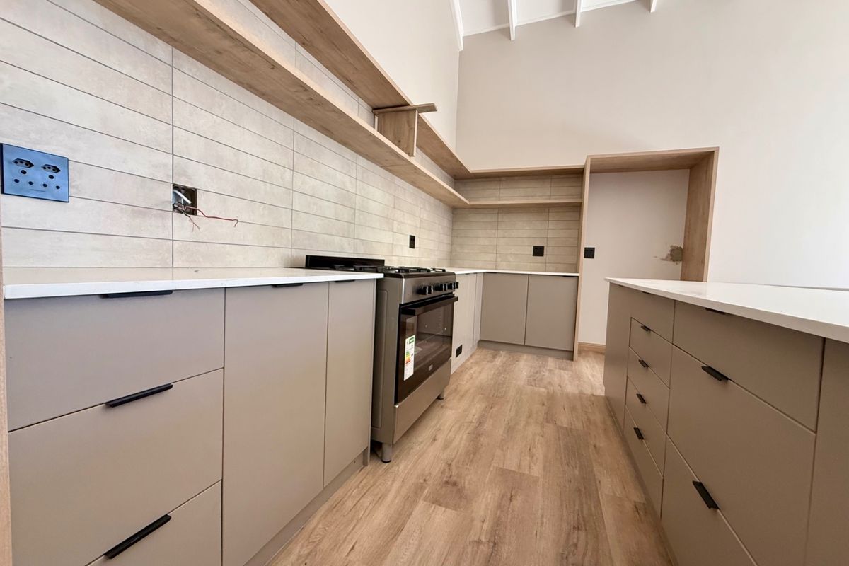 Modern kitchen featuring neutral cabinetry, stone countertops, open shelving, and a freestanding oven, set under a high vaulted ceiling with wood-look flooring.
