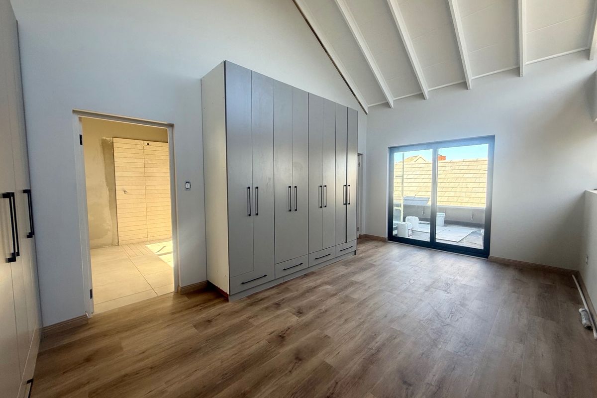 Spacious bedroom featuring vaulted ceilings with exposed rafters, modern laminate flooring, built-in cupboards, and a sliding door leading to an outdoor balcony area.