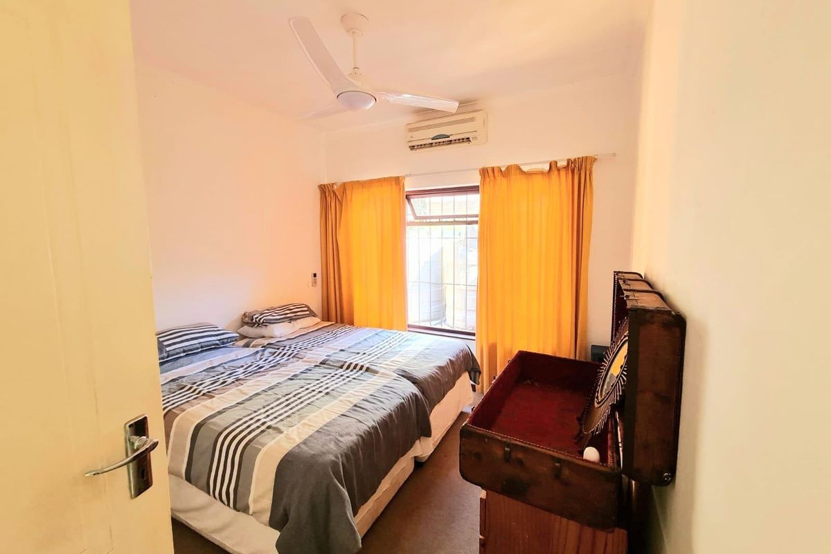 A functional bedroom featuring a ceiling fan, wall-mounted air conditioning unit, and window security bars.