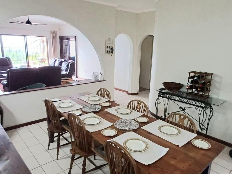Open-plan dining and living area featuring arched architectural details, tiled flooring, and access to an outdoor space through sliding glass doors.