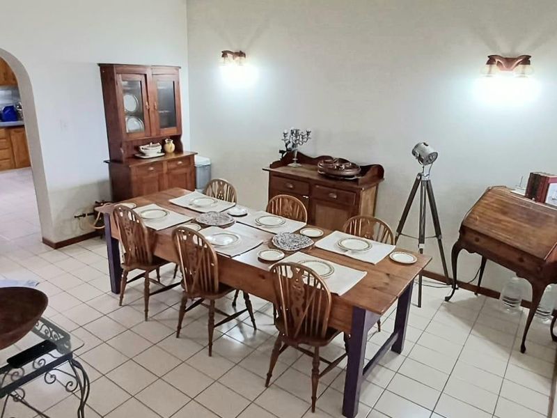 A dining room featuring ceramic tile flooring and an arched entryway leading to the kitchen, illuminated by wall-mounted light fixtures.