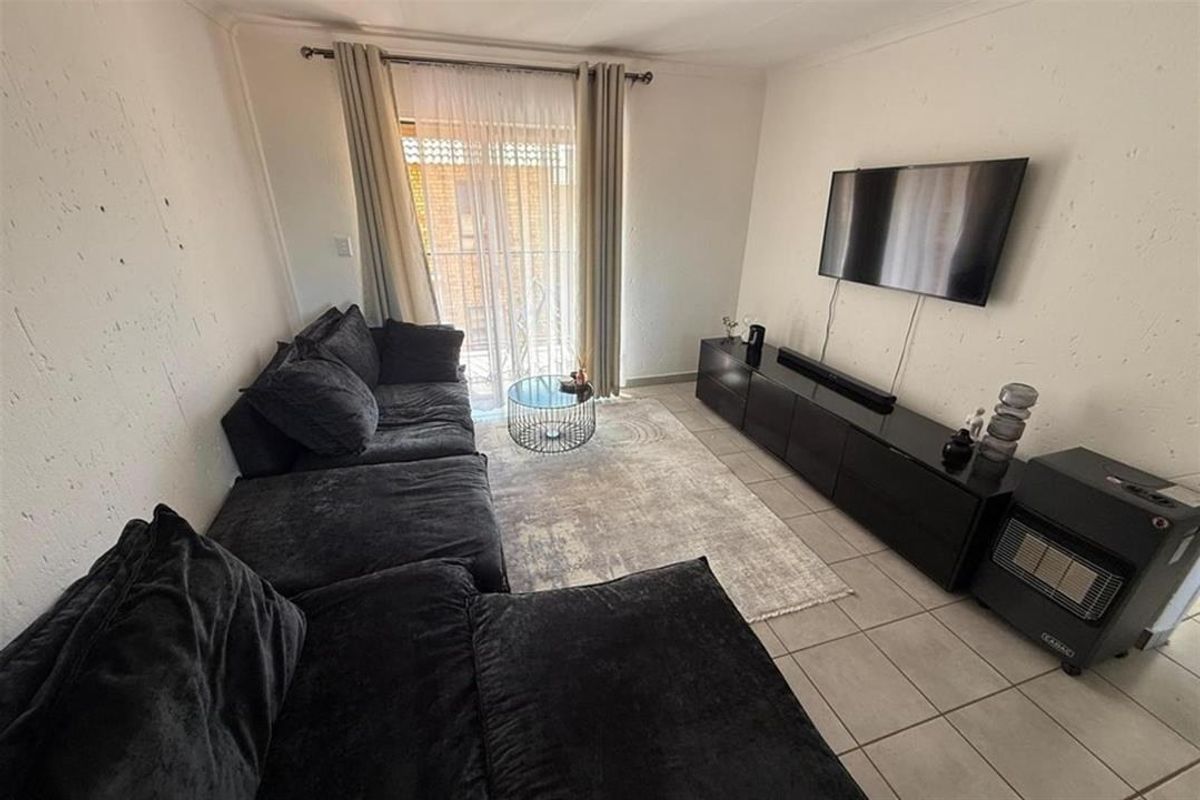 A living room featuring tiled flooring and a sliding glass door leading to a balcony, with visible wall plaster imperfections.