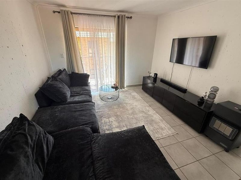 A living room featuring tiled flooring and a sliding glass door leading to a balcony, with visible wall plaster imperfections.