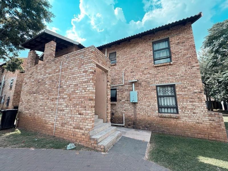 Rear exterior view of a face brick apartment building featuring a concrete staircase, security-barred windows, and an external gas geyser unit.