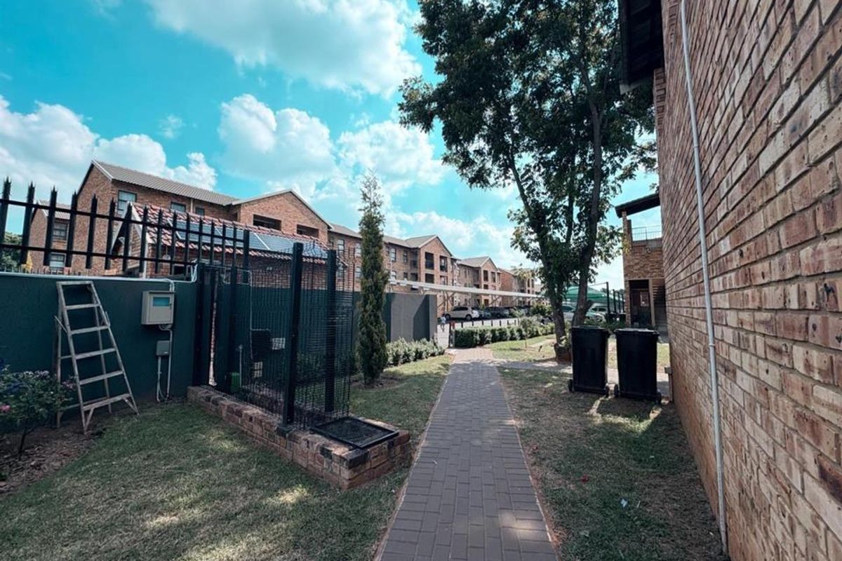 A view of the apartment complex exterior featuring a paved walkway, brick building facades, and secure perimeter fencing.