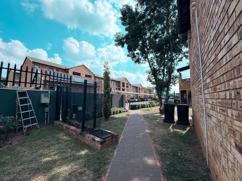 A view of the apartment complex exterior featuring a paved walkway, brick building facades, and secure perimeter fencing.