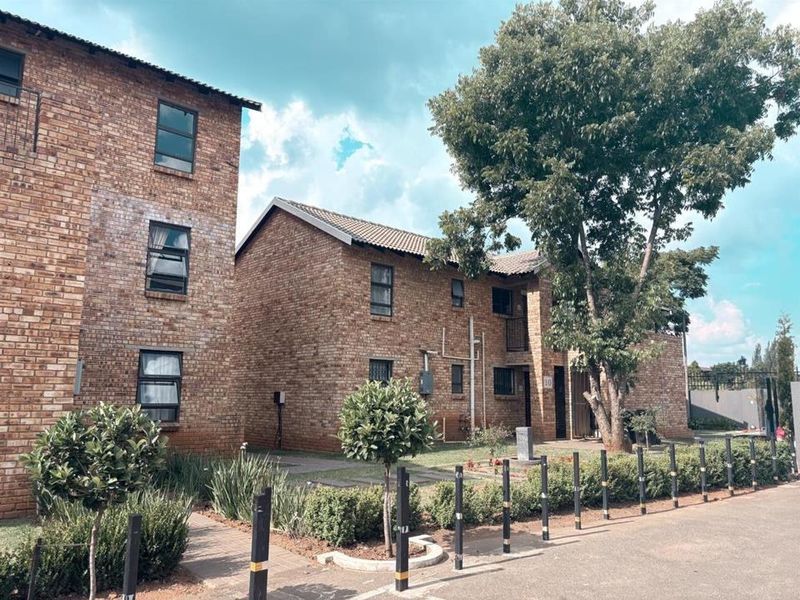 Exterior view of a multi-story face-brick apartment complex featuring a paved walkway, established trees, and landscaped garden areas.