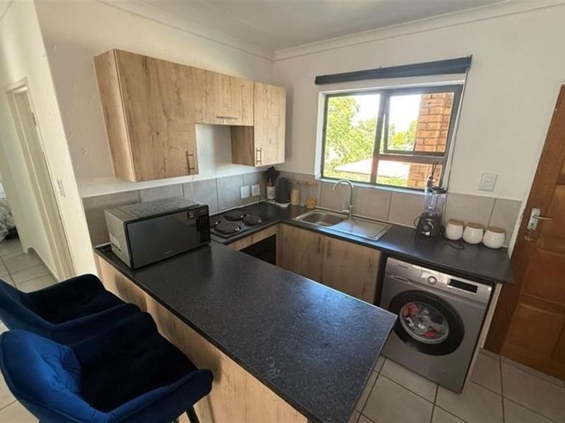 Compact kitchen featuring modern wood-look cabinetry, dark countertops, a built-in hob, and integrated laundry plumbing, offering a functional and efficient workspace.