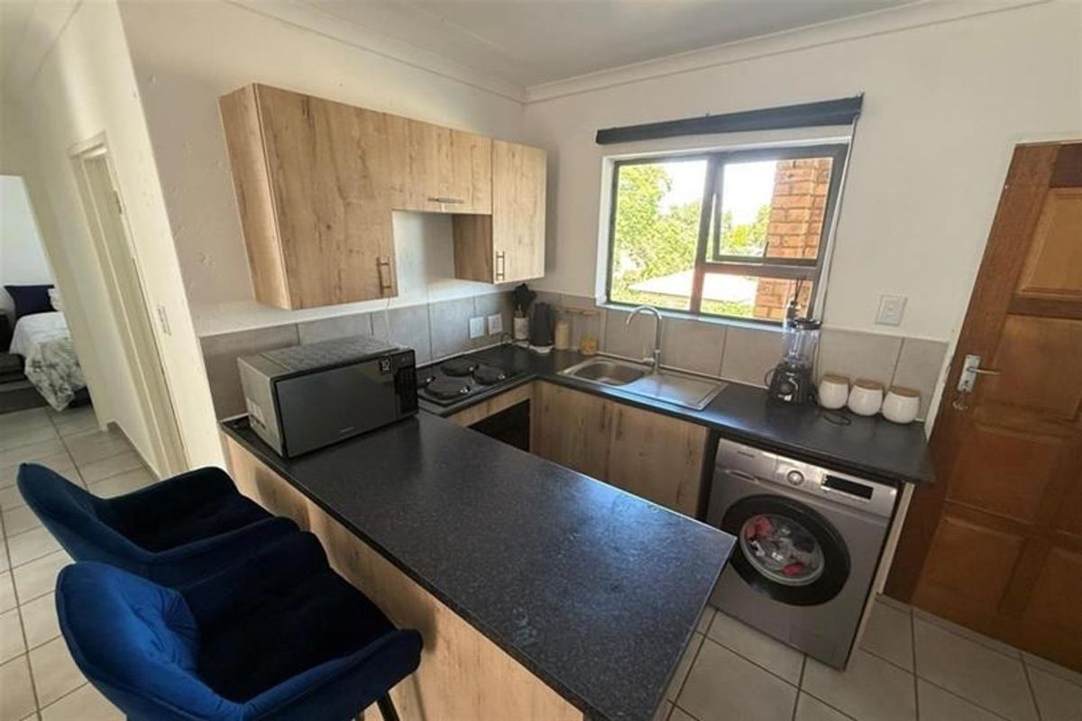 Compact kitchen featuring modern wood-look cabinetry, dark countertops, a built-in hob, and integrated laundry plumbing, offering a functional and efficient workspace.
