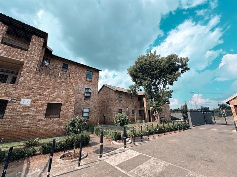 Exterior view of a multi-story face brick apartment complex featuring paved driveway access and established landscaping.