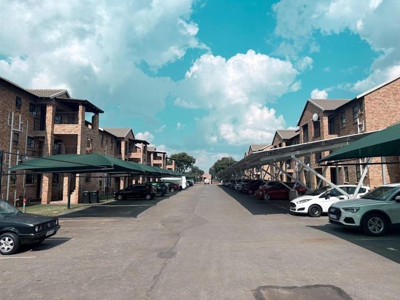 Exterior view of an apartment complex featuring brick buildings, paved driveway, and covered parking bays for residents.