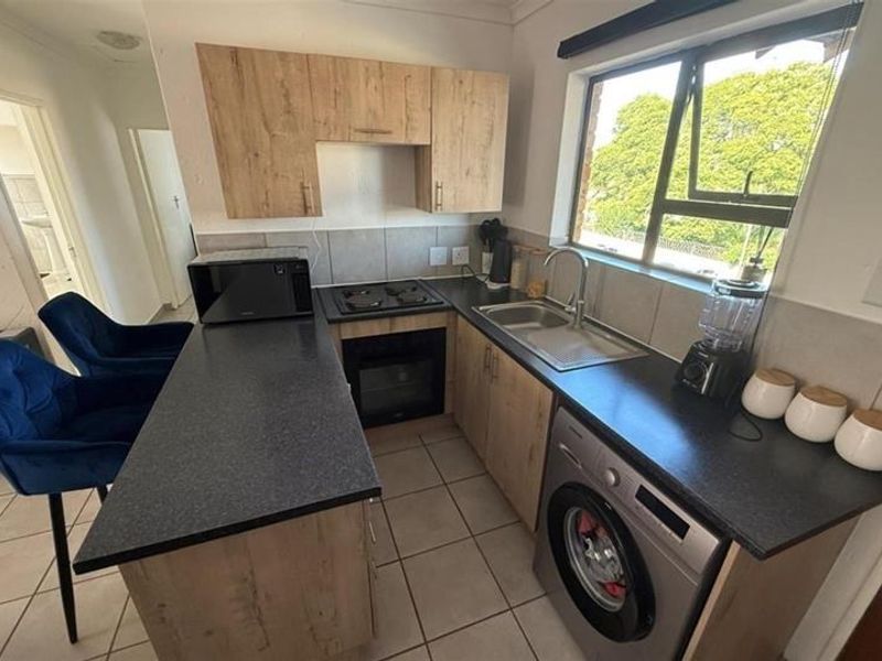 Compact kitchen featuring light wood-look cabinetry, dark countertops, built-in oven and hob, and a convenient breakfast bar for casual dining.