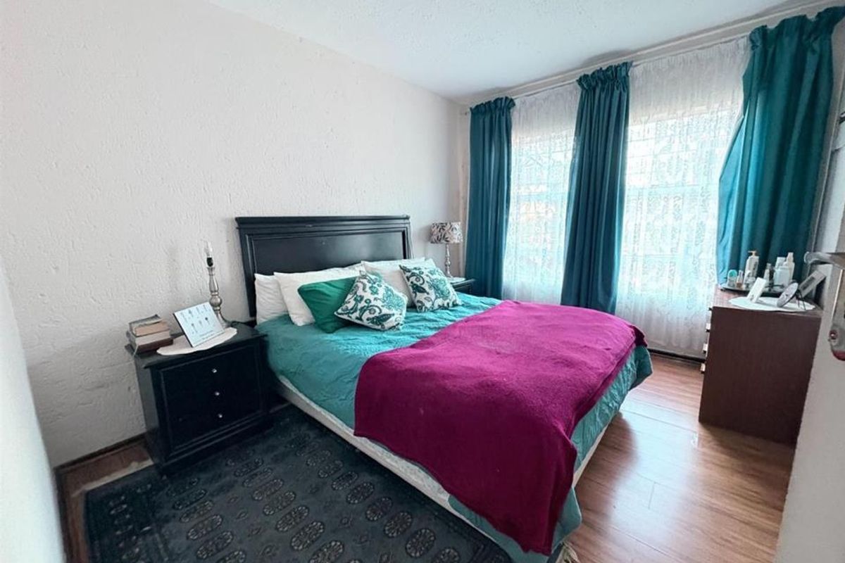 A bedroom featuring laminate flooring and textured walls, with large windows allowing natural light into the space.