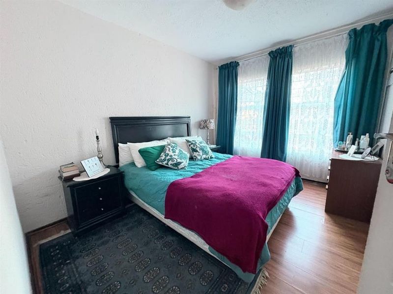 A bedroom featuring laminate flooring and textured walls, with large windows allowing natural light into the space.