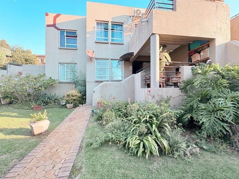 Front elevation of a multi-story apartment unit featuring a paved walkway, landscaped garden, and a private balcony.