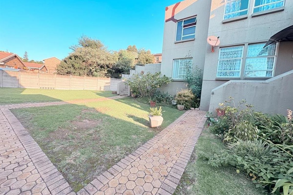 Rear exterior view of the apartment building featuring a paved walkway, lawn area, and perimeter boundary wall.