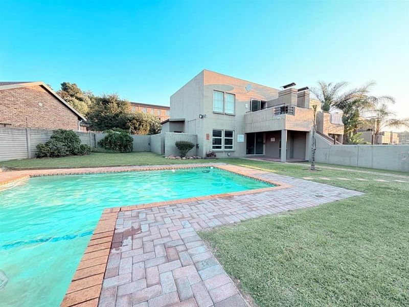 Exterior view of the apartment complex featuring a swimming pool, paved surround, and a private balcony overlooking the garden area.