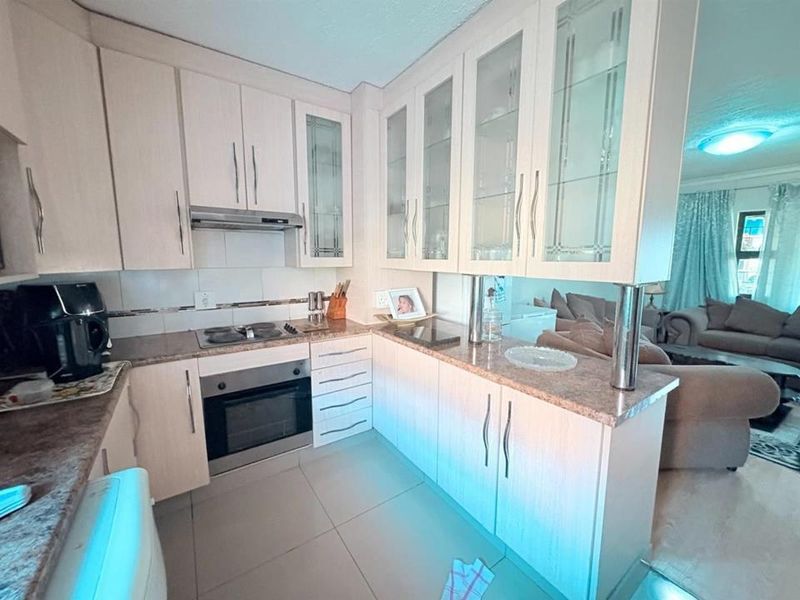 Open-plan kitchen featuring light-toned cabinetry, laminate countertops, integrated oven and hob, and tiled flooring, seamlessly connecting to the adjacent living area.