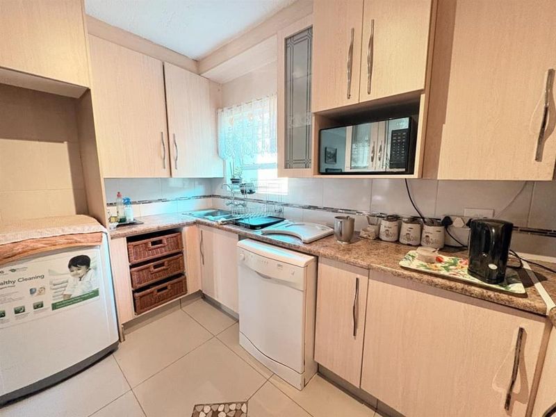 A functional kitchen featuring light wood-tone cabinetry, laminate countertops, tiled backsplash, and tiled flooring with space for under-counter appliances.