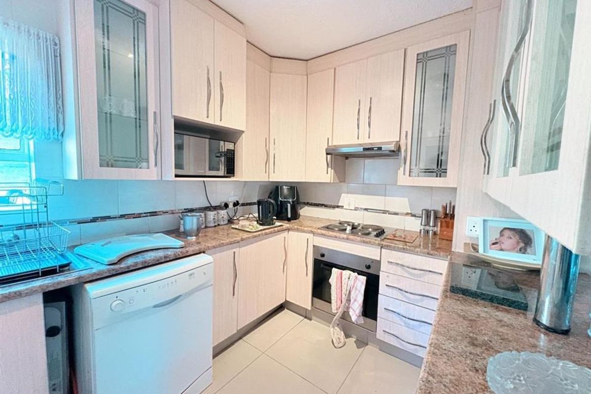 A functional kitchen featuring light wood-finish cabinetry, granite countertops, built-in oven, hob, extractor fan, and tiled flooring.