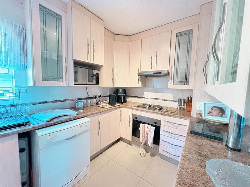 A functional kitchen featuring light wood-finish cabinetry, granite countertops, built-in oven, hob, extractor fan, and tiled flooring.