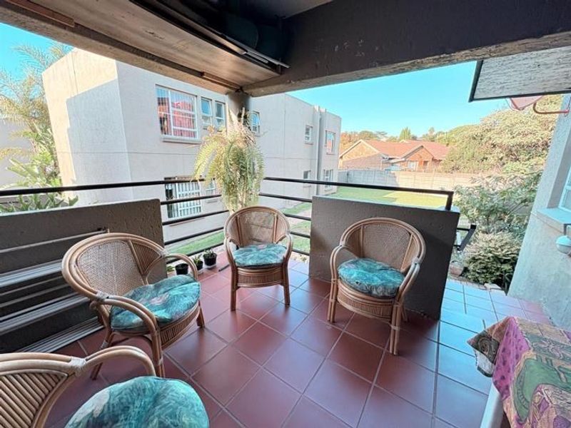 A covered balcony featuring tiled flooring and metal railings, overlooking the surrounding apartment complex grounds.