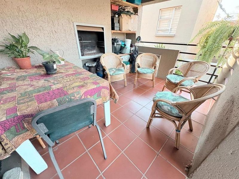Covered balcony featuring a built-in braai, tiled flooring, and metal balustrade, offering a functional outdoor entertainment space.