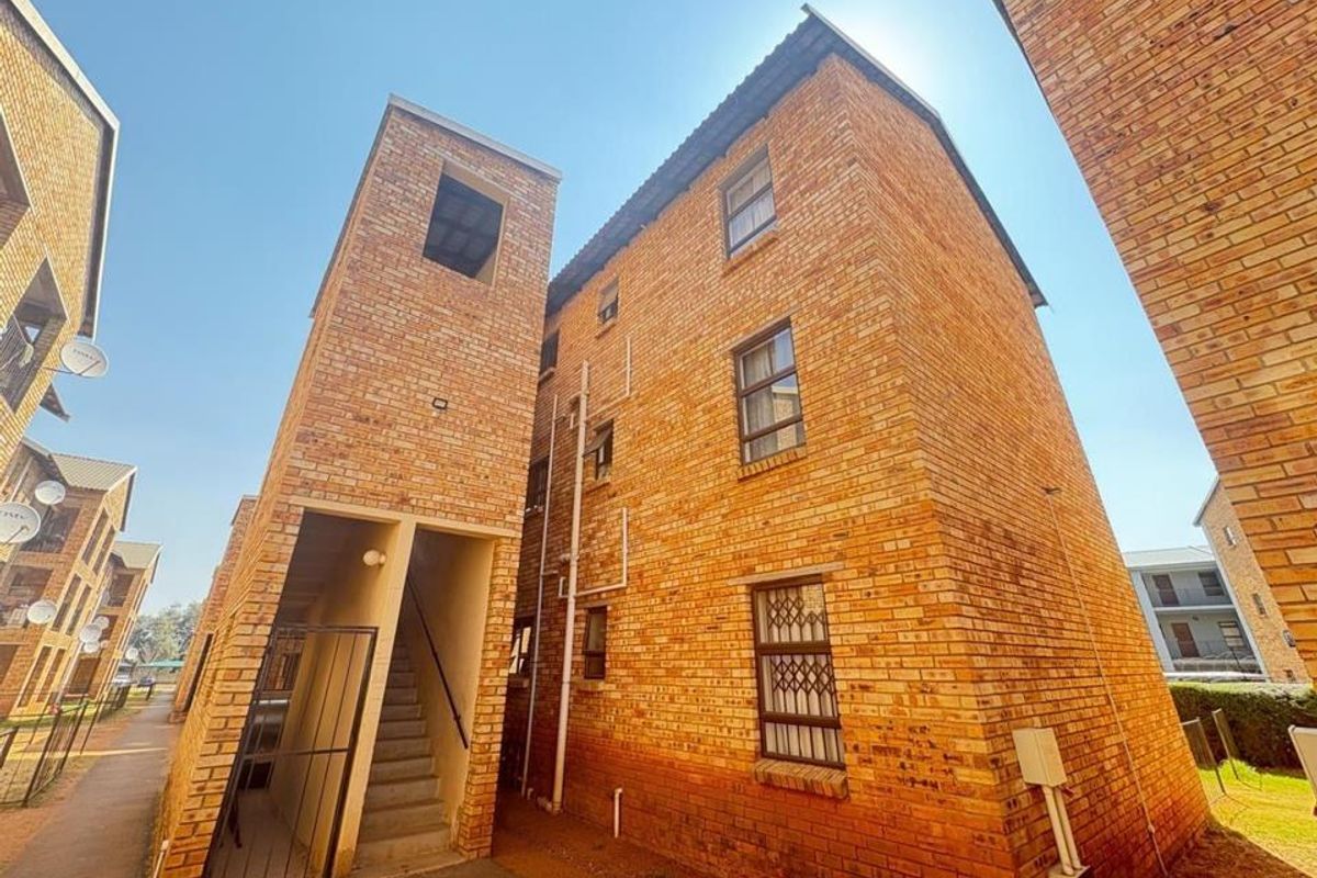 Exterior view of a multi-story face brick apartment building featuring an external stairwell and security-fitted windows.