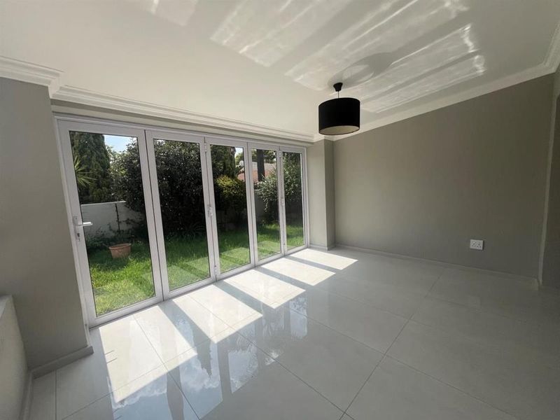 Bright living area featuring large bi-fold glass doors opening to the garden, finished with polished porcelain floor tiles and modern cove cornicing.