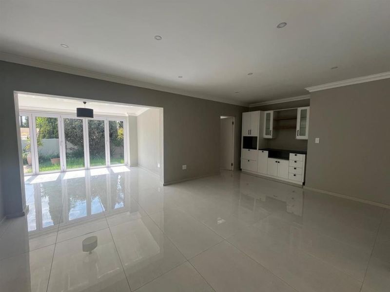 Spacious open-plan living area featuring polished porcelain tiles, recessed lighting, and bi-fold doors opening to the garden, complemented by built-in cabinetry.