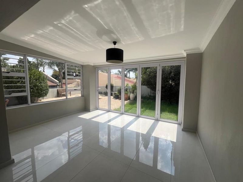 Bright and spacious living area featuring polished tiled floors, modern aluminium stacker doors opening to the garden, and large windows providing ample natural light.