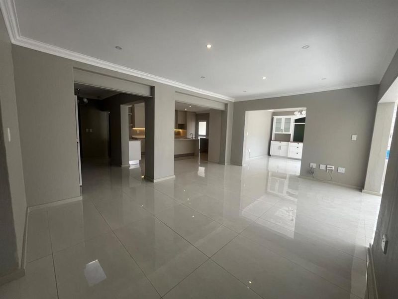 Spacious open-plan living area featuring polished porcelain floor tiles, recessed downlighting, and neutral wall finishes, seamlessly connecting to the kitchen and dining spaces.