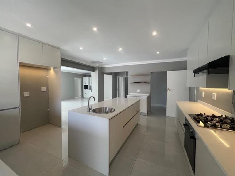 Modern, spacious kitchen featuring a central island with an undermount sink, built-in oven, gas hob, extractor fan, and sleek cabinetry with recessed lighting.