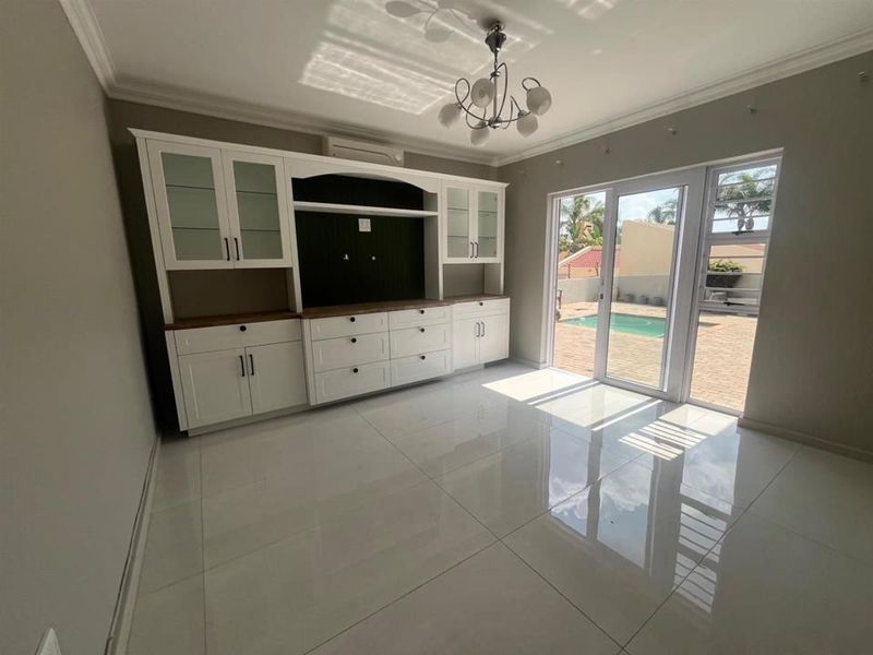 Bright living room featuring built-in cabinetry, polished tile flooring, and glass sliding doors providing direct access to the outdoor pool area.