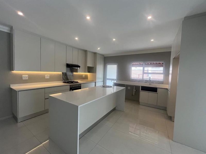 Modern, spacious kitchen featuring sleek cabinetry, stone countertops, a central island, integrated gas hob, and high-quality tiled flooring with recessed lighting.