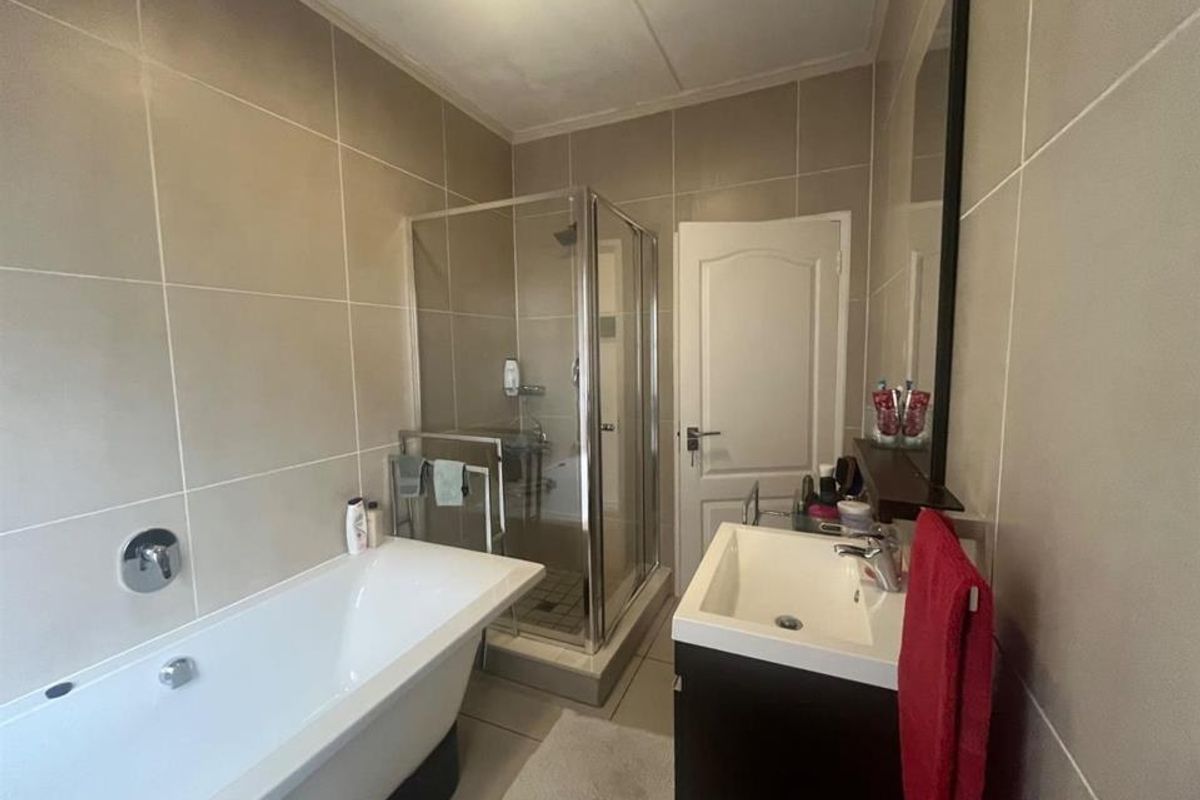 A well-maintained bathroom featuring a freestanding bathtub, a separate glass-enclosed shower, and a modern vanity unit with neutral wall tiling.