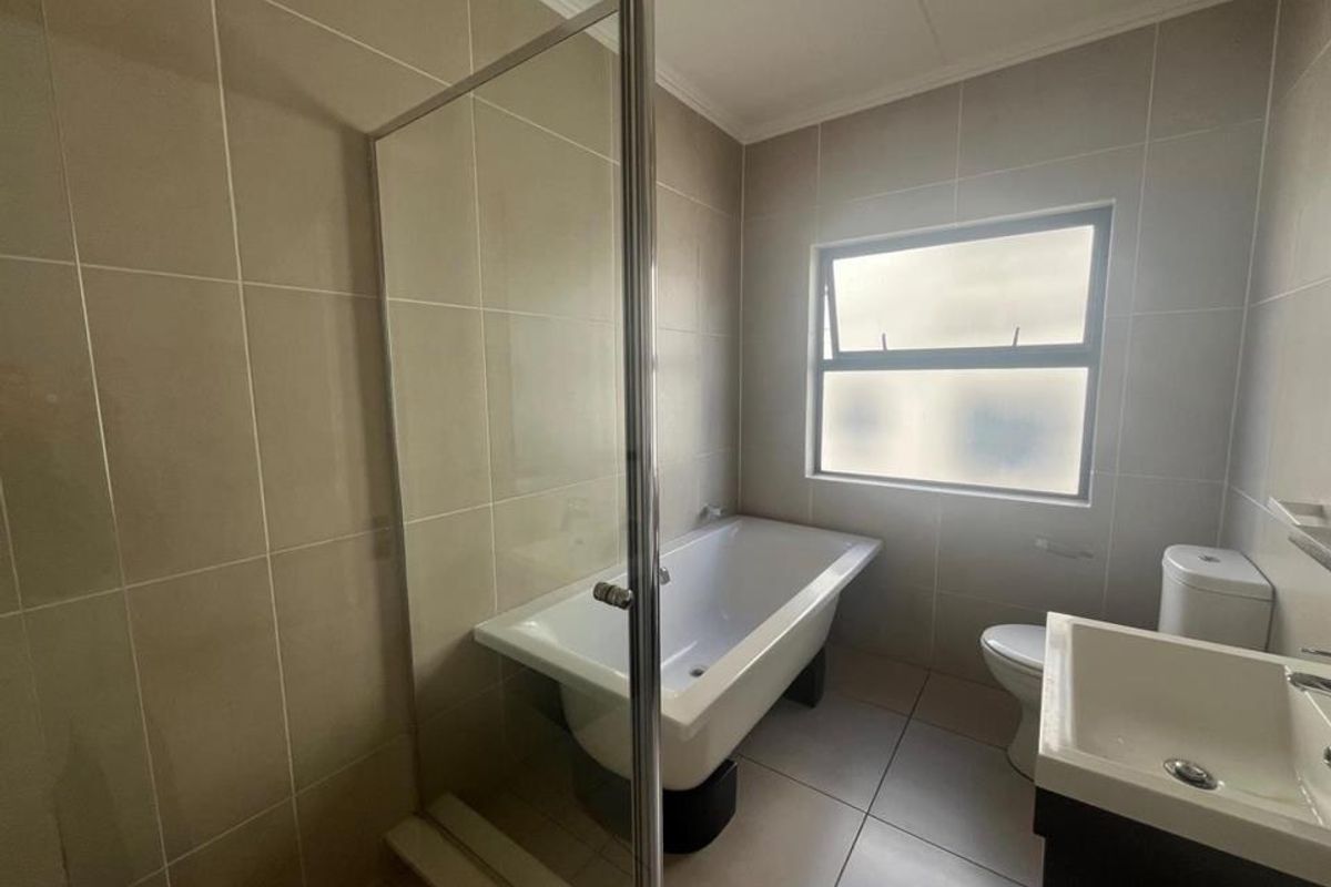 A clean, modern bathroom featuring a freestanding bathtub, separate glass shower enclosure, vanity basin, and neutral ceramic tiling throughout.