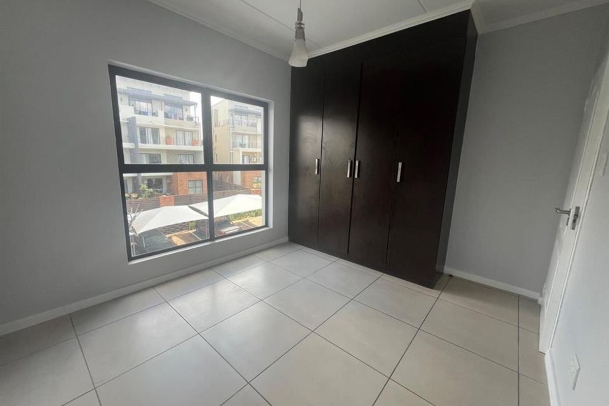 A bright, empty bedroom featuring neutral tiled flooring, light grey walls, and dark wood built-in cupboards.