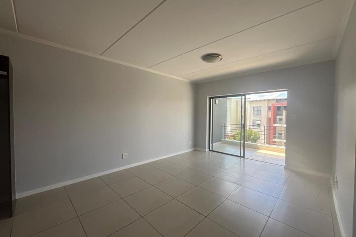 A bright, empty living room featuring neutral tiled flooring and a sliding glass door that opens onto a private balcony.